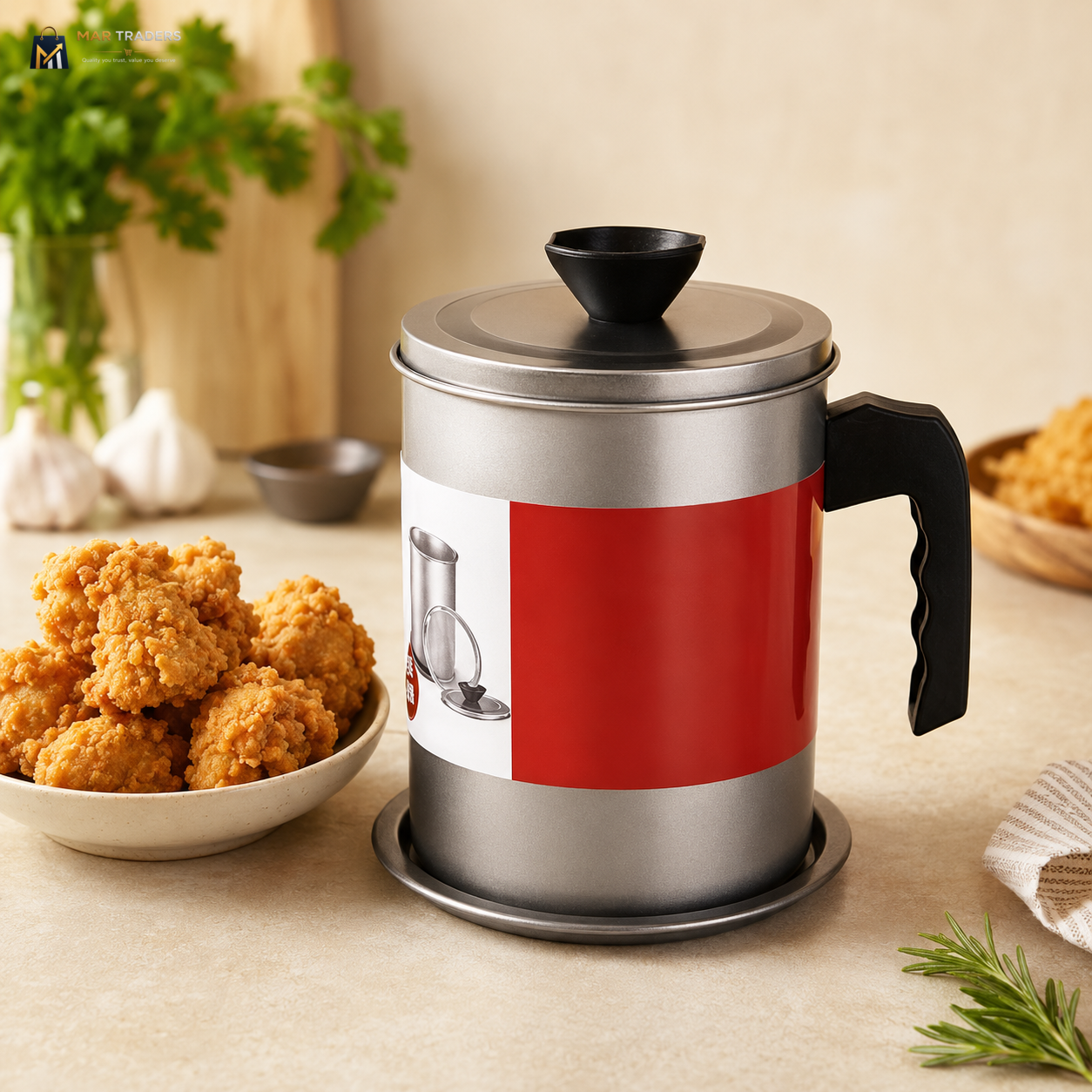 A stainless steel oil stainer with a red and white label wrap, shown on a beige tabletop with a bowl of fried chicken and kitchen herbs in the background.
