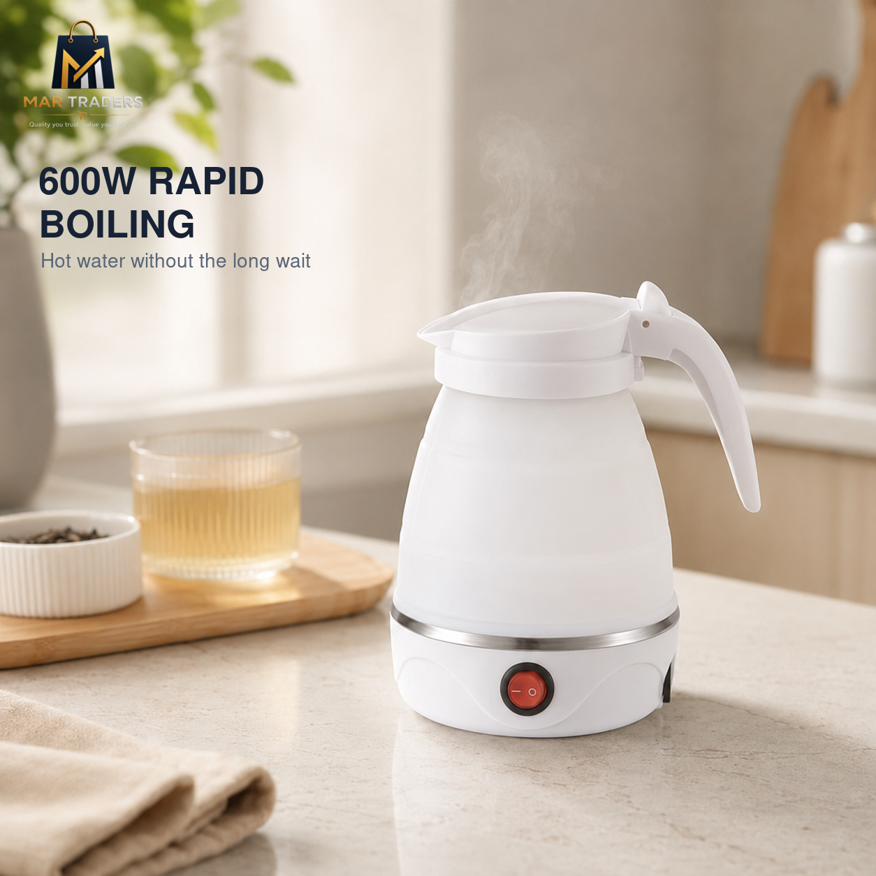 A white electric kettle with a curved handle sits on a light countertop, with steam rising from the top. A glass cup of tea and a small dish are on a wooden tray nearby, and a kitchen background is softly blurred.