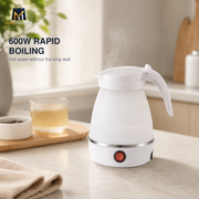 A white electric kettle with a curved handle sits on a light countertop, with steam rising from the top. A glass cup of tea and a small dish are on a wooden tray nearby, and a kitchen background is softly blurred.