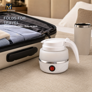 A white portable electric kettle with a handle and power button, shown next to an open suitcase and a travel tumbler on a beige carpet. Text on the image reads 'FOLDS FOR TRAVEL' and shows the MAR TRADERS logo.