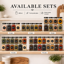 A set of clear food-grade glass spice jars with black lids and black circular labels, arranged on wooden shelves under the heading 'AVAILABLE SETS.' The image shows labeled set sizes from 4 jars to 16 jars, with examples of spices visible inside.