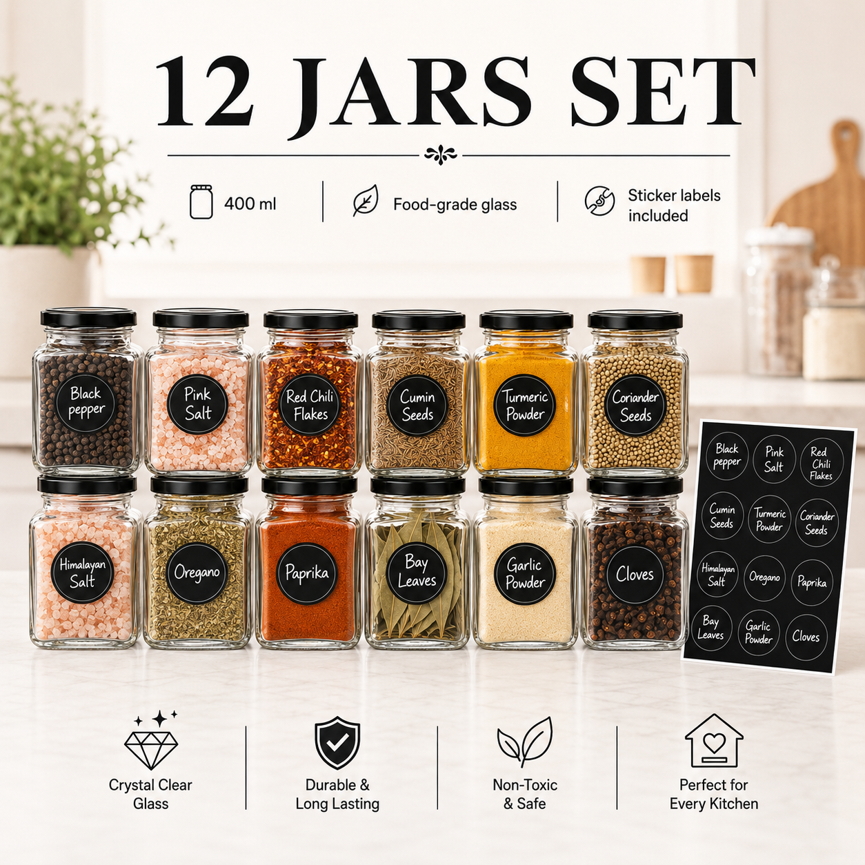 A 12-jar spice set arranged in two rows on a light countertop, with a blurred kitchen background. The jars are clear food-grade glass with black lids and labeled with black circular stickers showing spice names such as black pepper, pink salt, red chili flakes, cumin seeds, turmeric powder, coriander seeds, masala salt, oregano, paprika, bay leaves, garlic powder, and cloves.