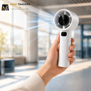 A hand holding a compact white handheld fan with a circular head, shown in a bright modern indoor setting with blurred windows and light rays. The MAR TRADERS logo appears in the top-left corner.