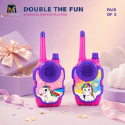Two pink and purple toy walkie-talkies with colorful unicorn designs, displayed on a pastel purple background with gift boxes and decorative props. Text at the top reads 'DOUBLE THE FUN' and 'PAIR OF 2'.