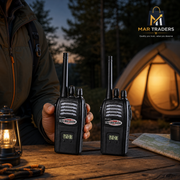 Two black Mar Traders walkie-talkies held by a person at a campsite table, with a glowing tent, lantern, and trees in the background. The Mar Traders logo is visible in the top right corner.