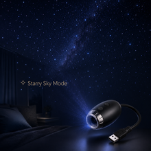 A small black USB projector shown on a bedside table in a dim bedroom, casting a starry sky pattern across the wall above a bed. The text 'Starry Sky Mode' appears on the left, and the projector has a USB cable attached.